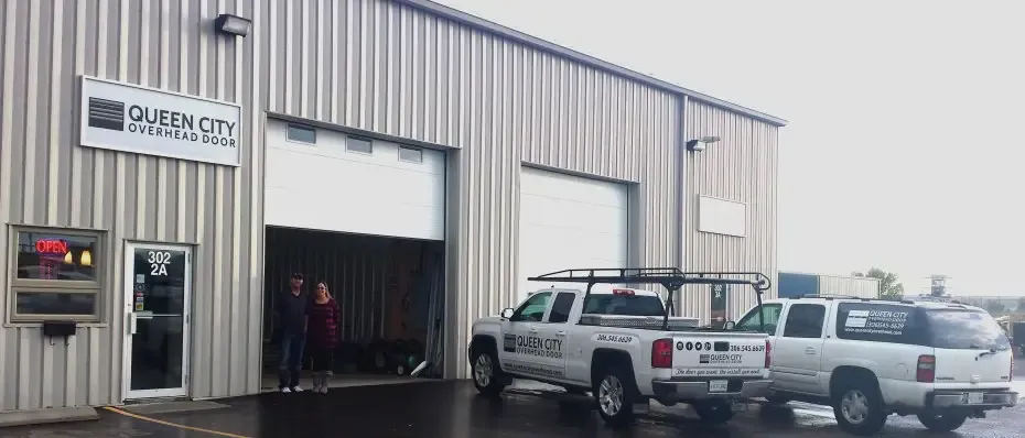 Queen City Garage Doors Regina with two white company trucks parked outside, and an open garage door with two people standing nearby.